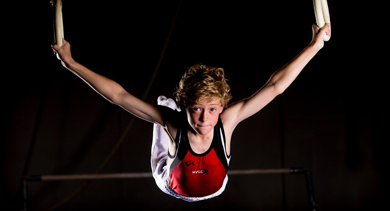 boy gymnast in action on rings black backgroung