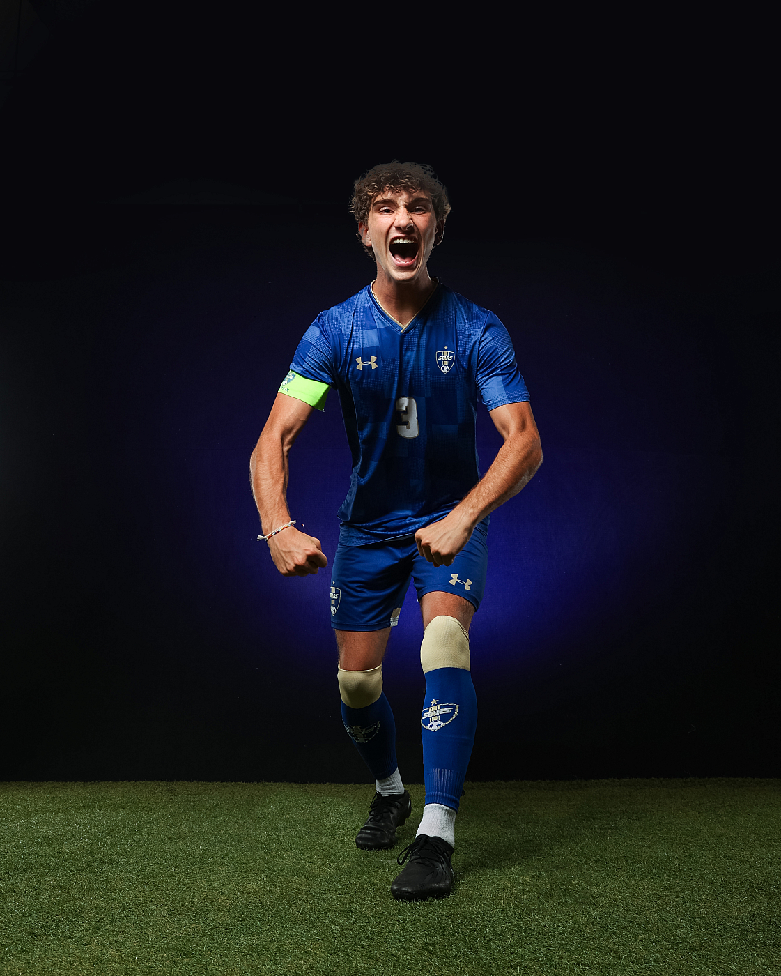 Teenage boy in blue soccer uniform poses with intense face for sports portrait.
