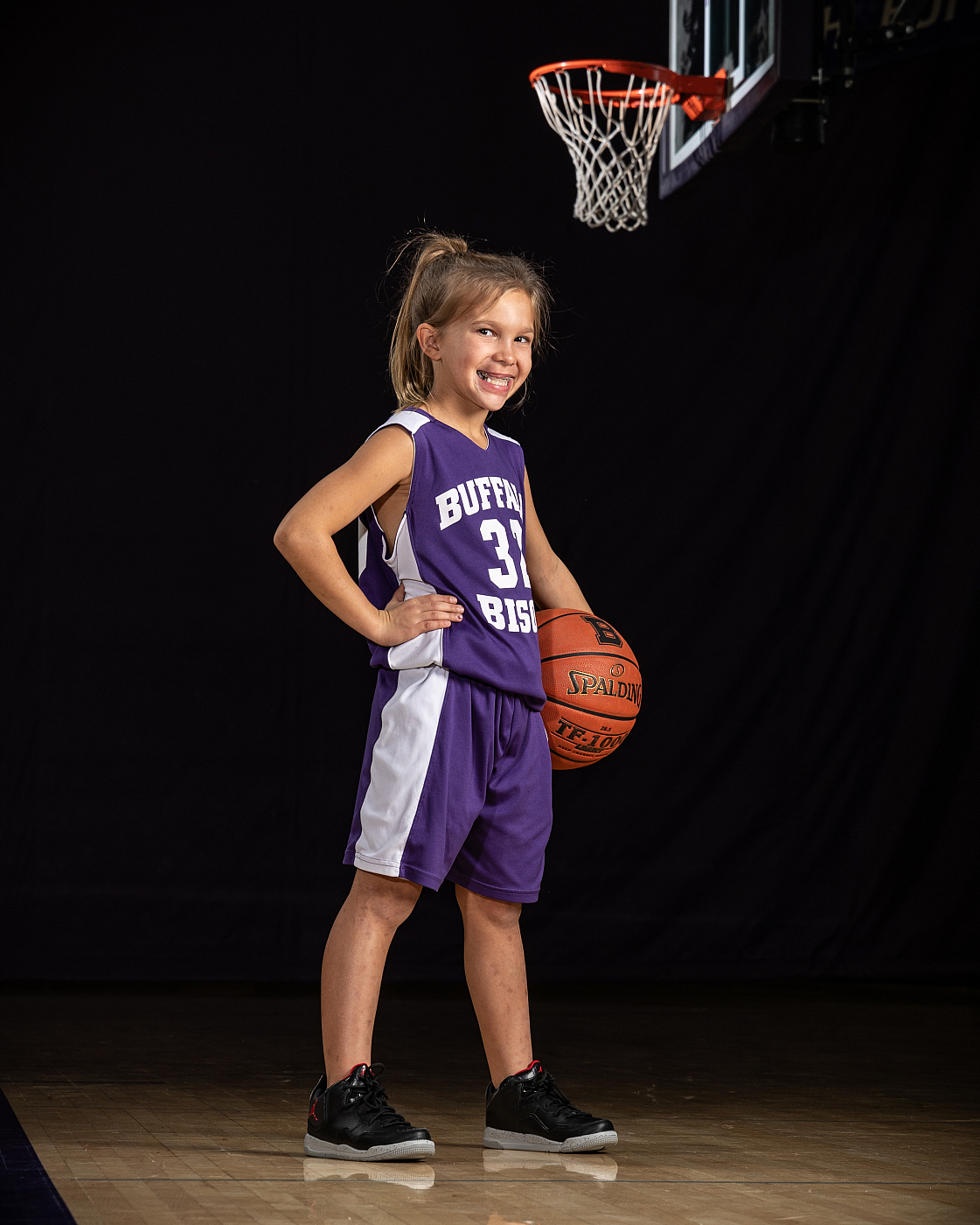 Girl basketball sports portrait in front of basket wearing purple Buffalo Bison uniform.