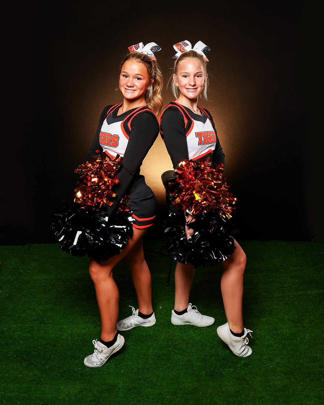 Two girl cheerleaders sports buddy portrait. Black, white, and orange cheer uniforms.