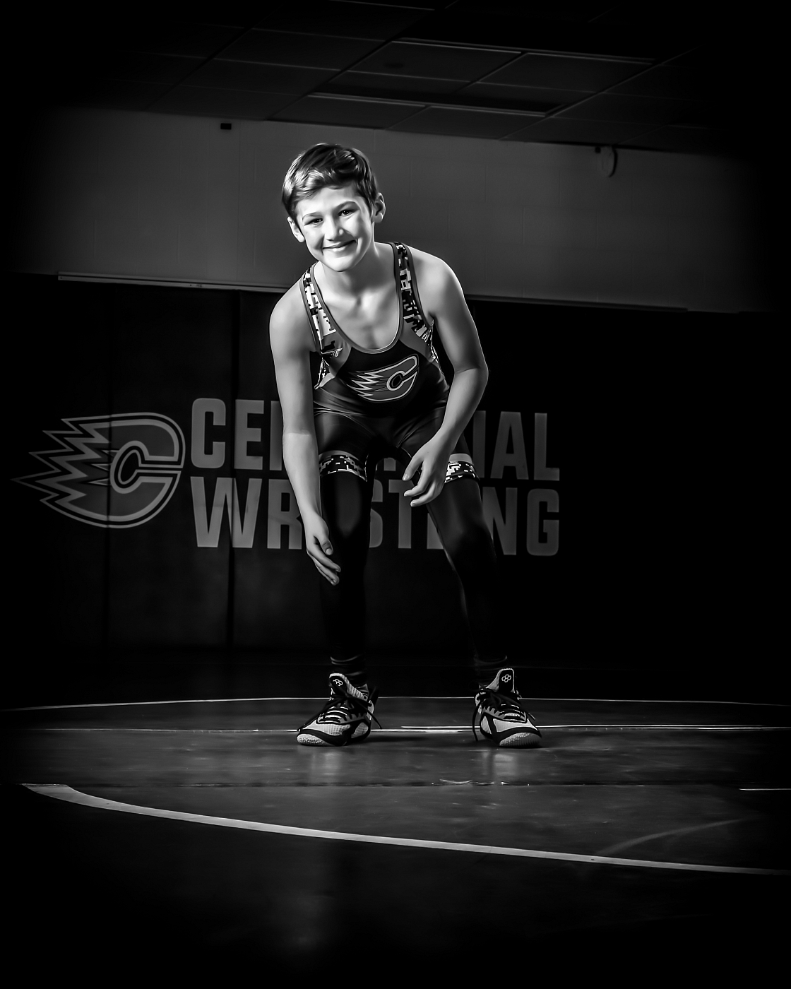 Black and white wrestling portrait with boy posed on wrestling mat.