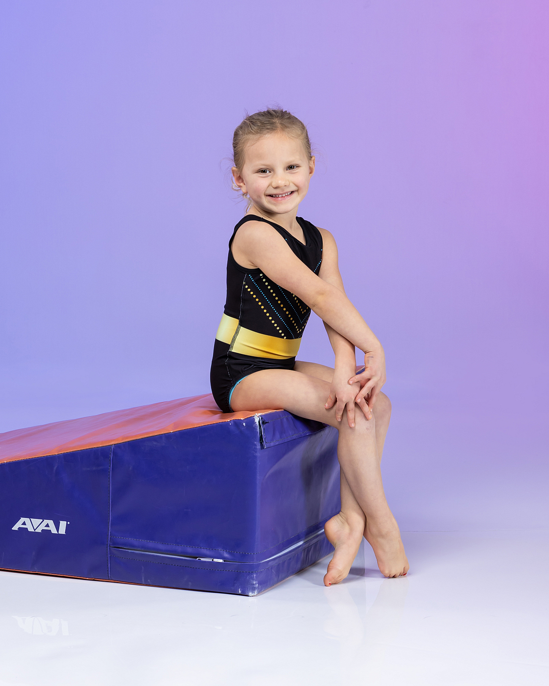 Cute little girl sitting on gymnastics mat, purple background, gymnastics portrait.