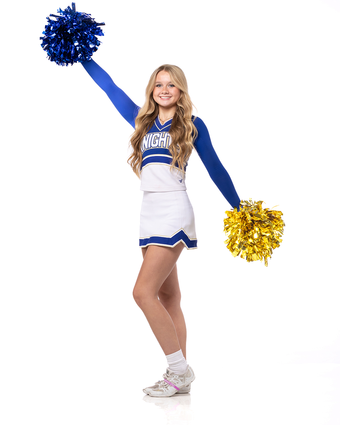 Teenage girl in blue and white cheerleading uniform posing with pom poms for cheer portrait, white background.