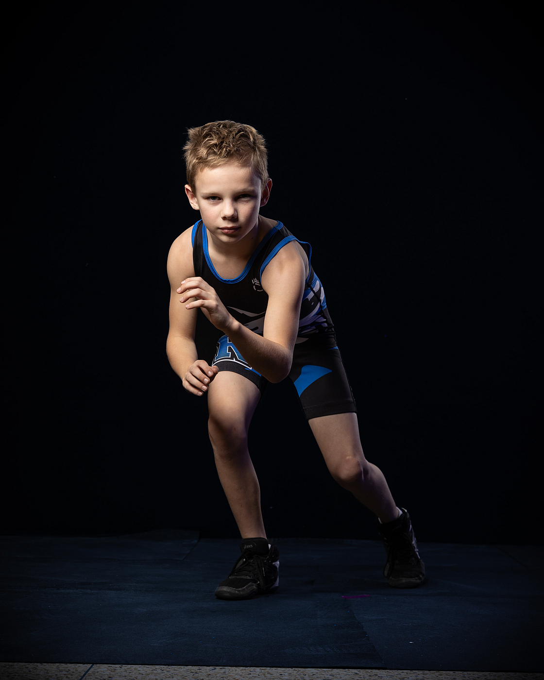 Little boy posed wrestling portrait on wrestling mat wearing blue uniform