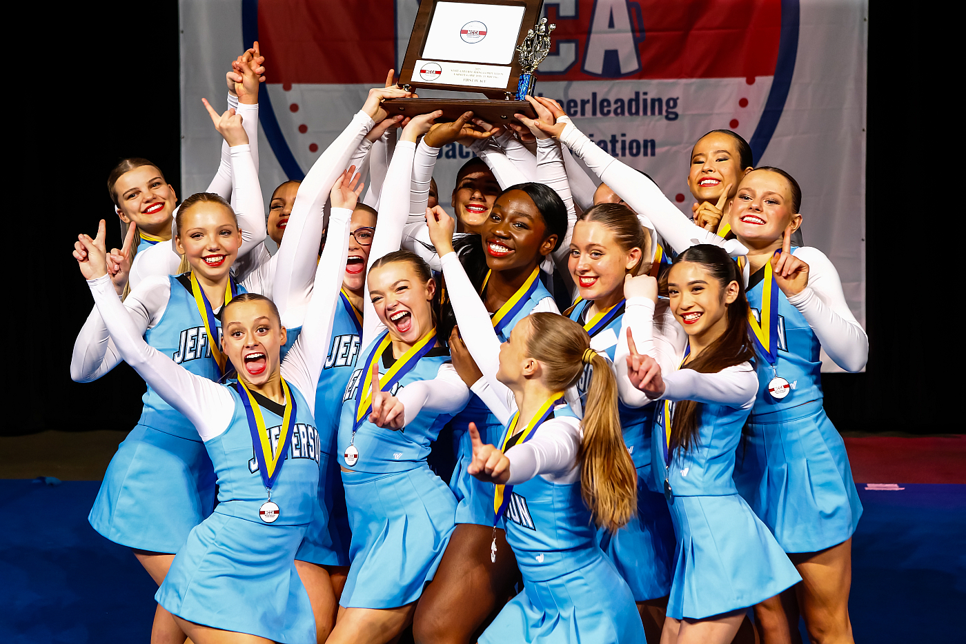 girls mn cheerleading team in blue uniforms holding up trophy 