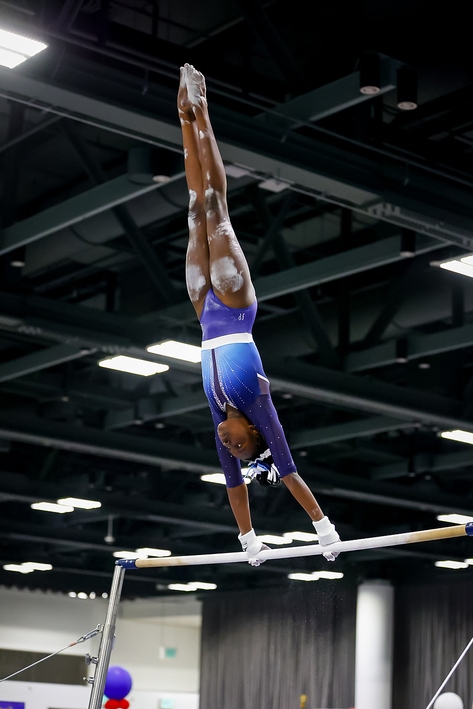 high school girl gymnast in purple and blue leotard upside down pike on bars