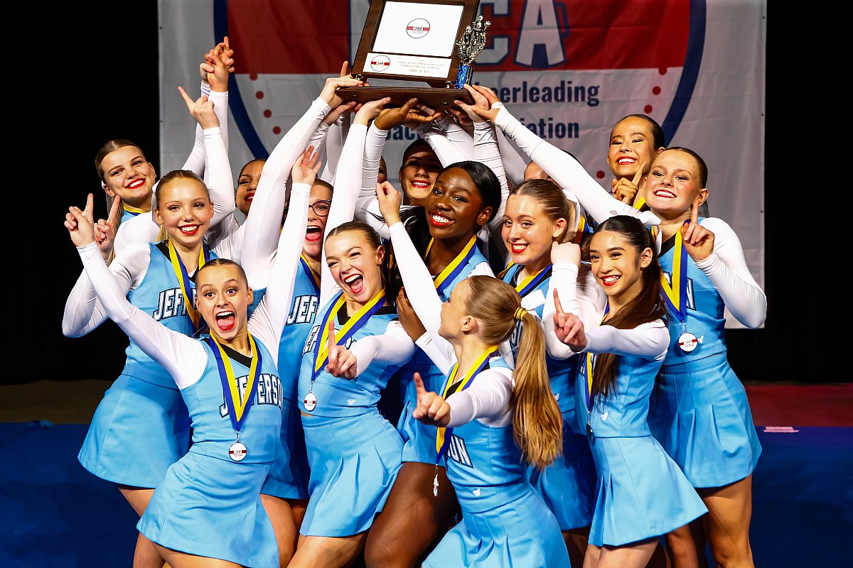 girls mn cheerleading team in blue uniforms holding up trophy 