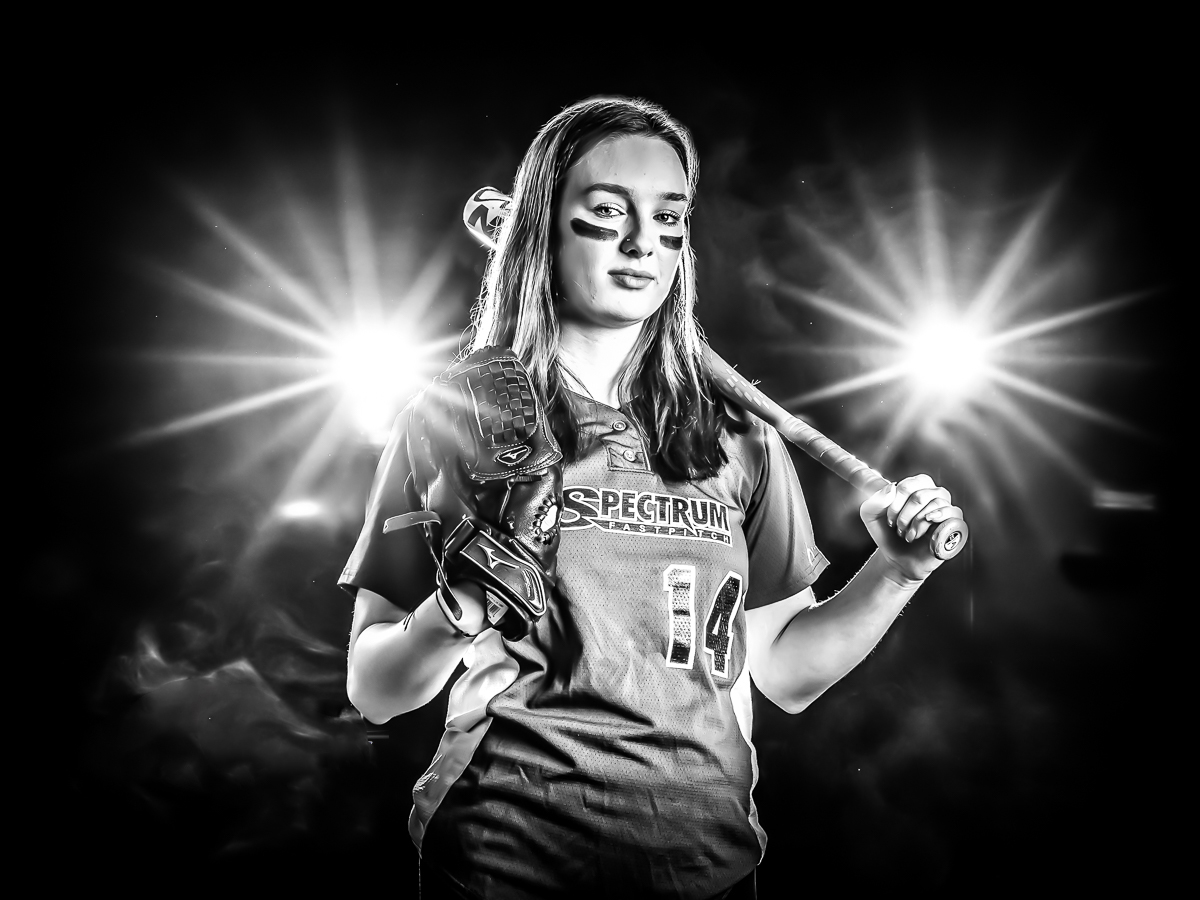 blak and white softball portrait of girl holding bat and glove, stadium lights in background
