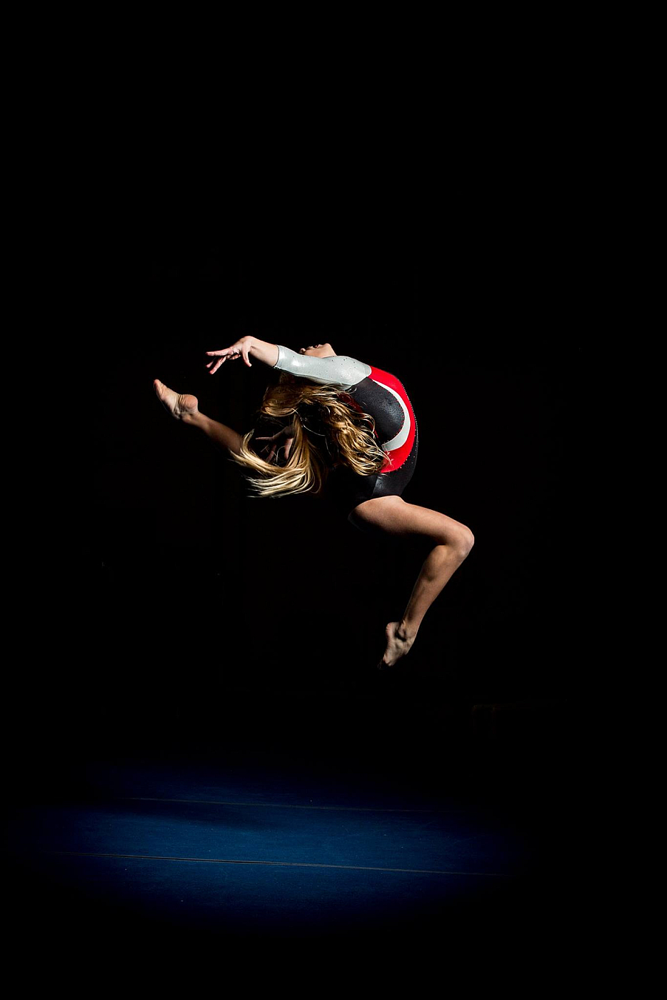 gymnast leaping in air black background, blonde hair