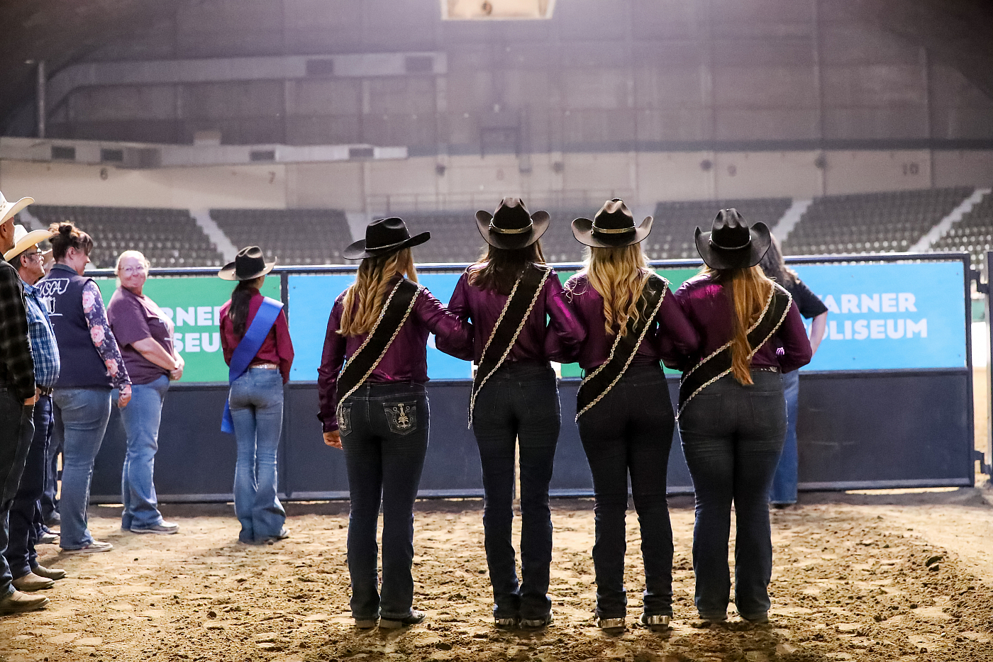 four women dressed in purple shirts and black cowboy hats stand for national anthem at horse show
