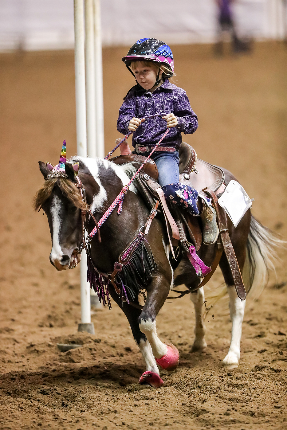 litter girl rides on brown pony in purple shirt