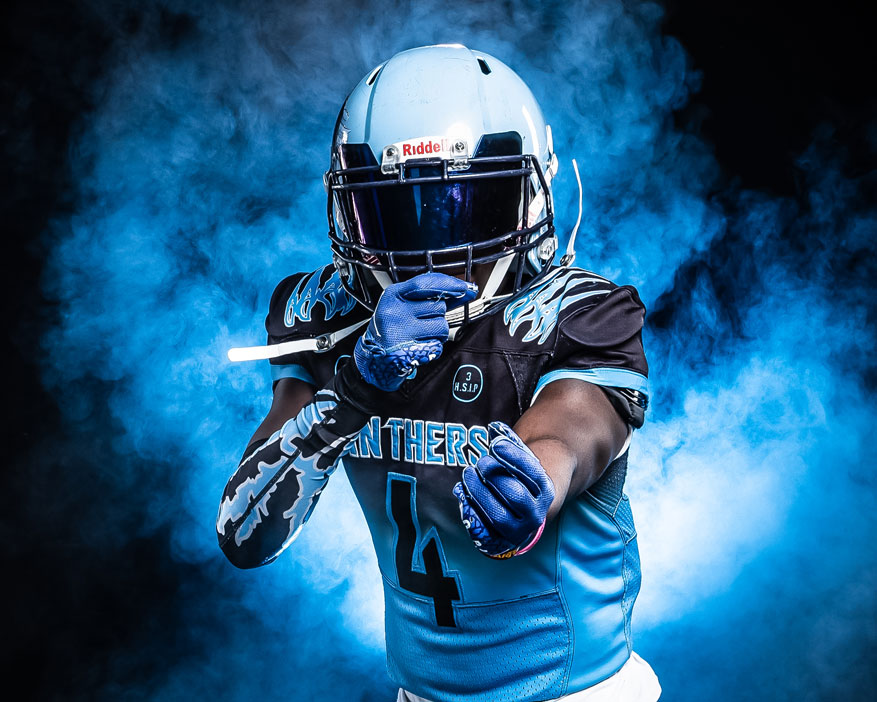 football player in blue uniform gesturing at camera with blue smoke in background