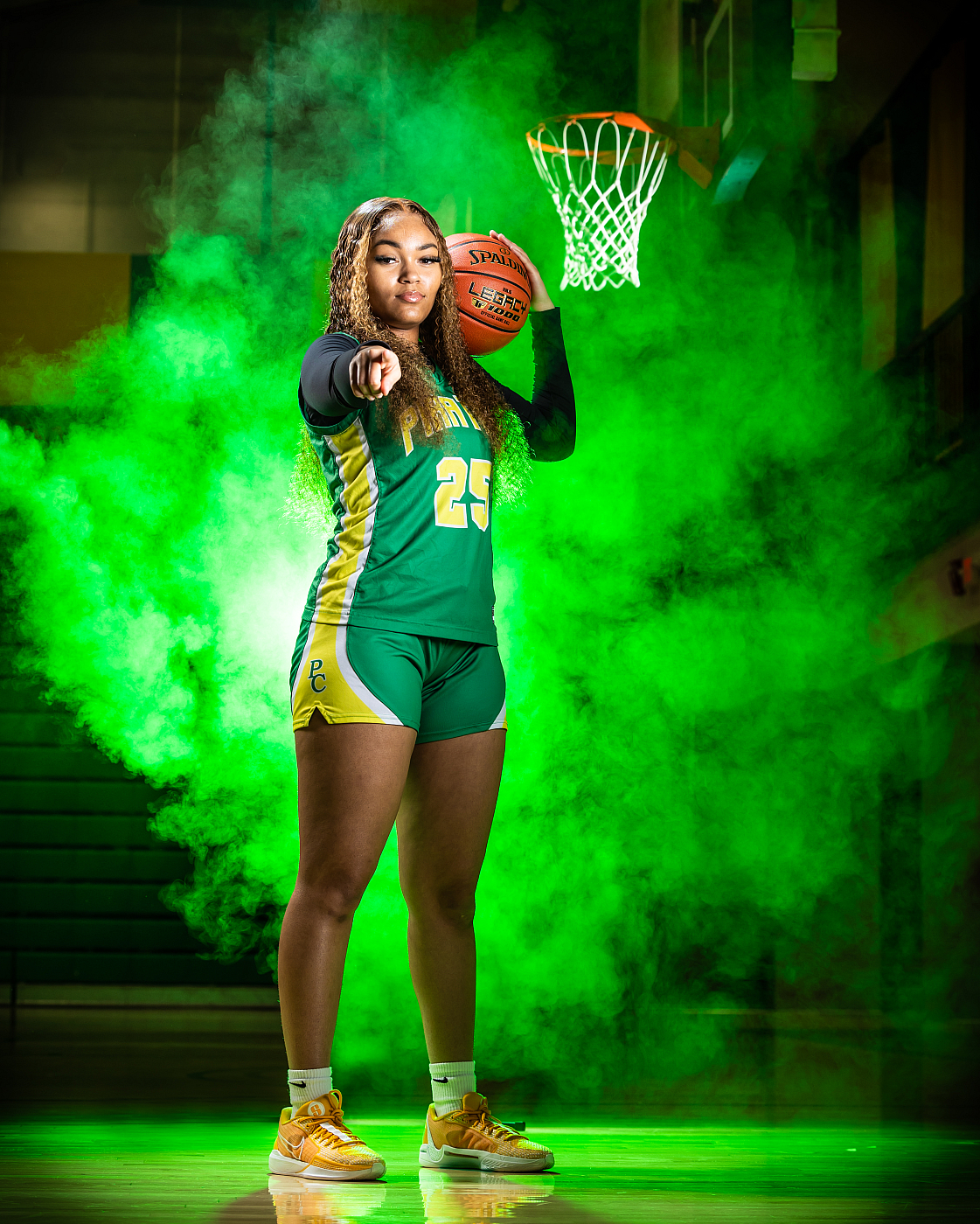 high school girl basketball player pointing at camera with basketball, green smoke background