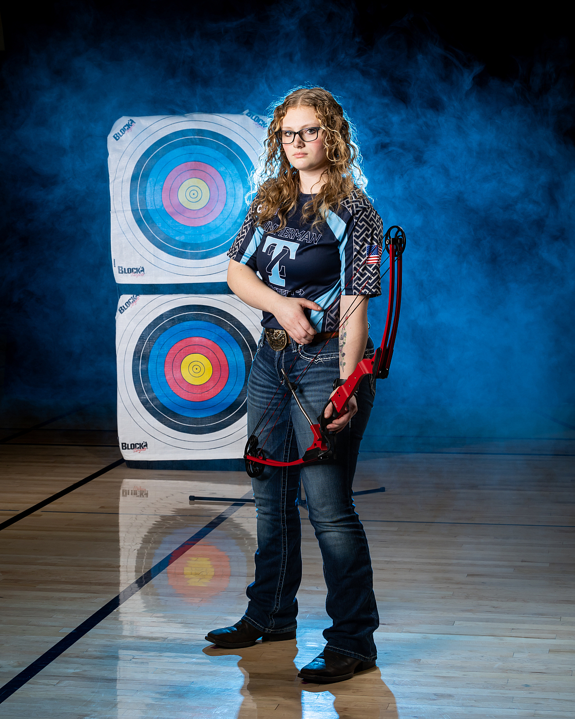 girl holding bow and arrow archery specialty portrait with targets and blue smoke in background