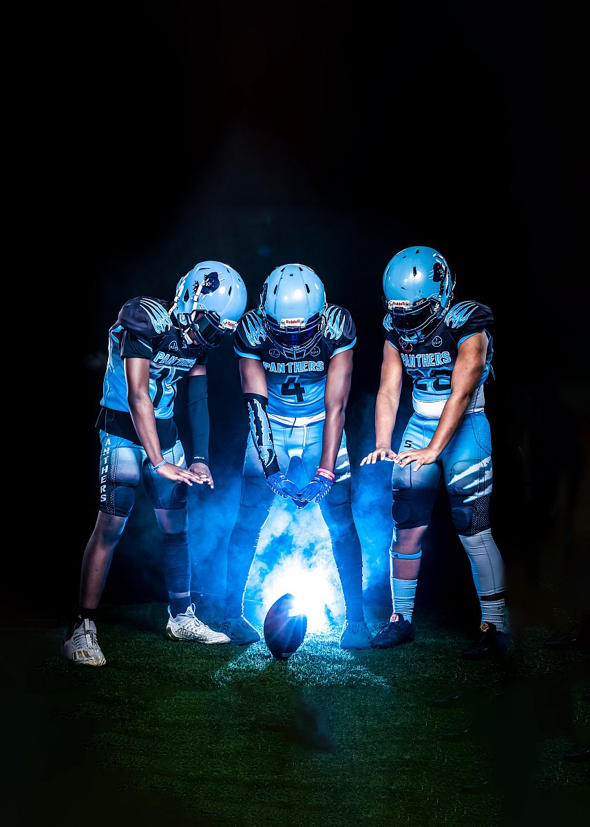 three football players standing over football with lights and blue smoke in background
