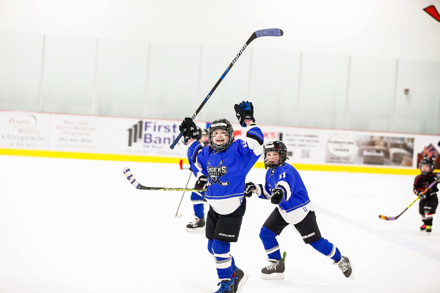 young boy hockey player in blue uniform raising hockey stick in air and cheering during hockey game. Live action photography during hockey tournament.