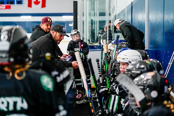 young boy hockey team on bench while the coach talks to them before hockey game